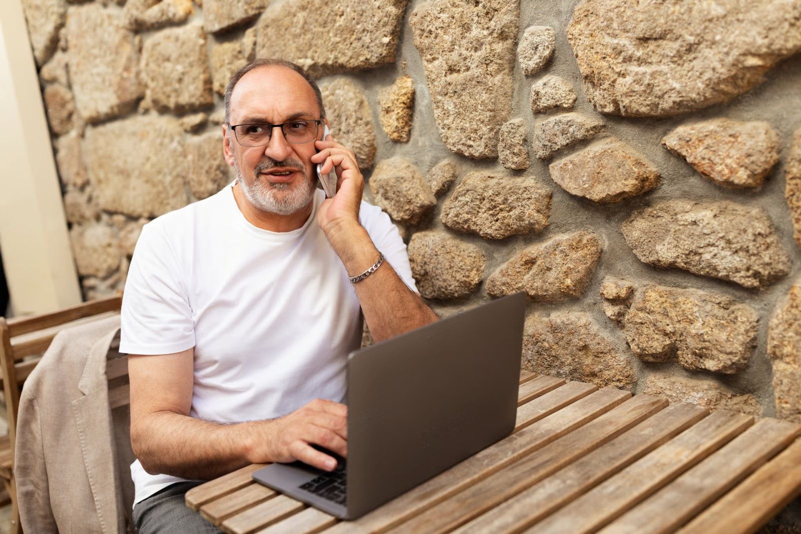 Un hombre habla por teléfono mientras usa su computadora portátil en casa
